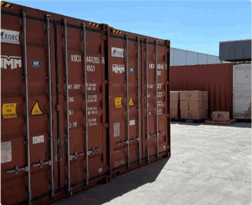 Shipping containers in a yard beside stacked cartons on pallets.